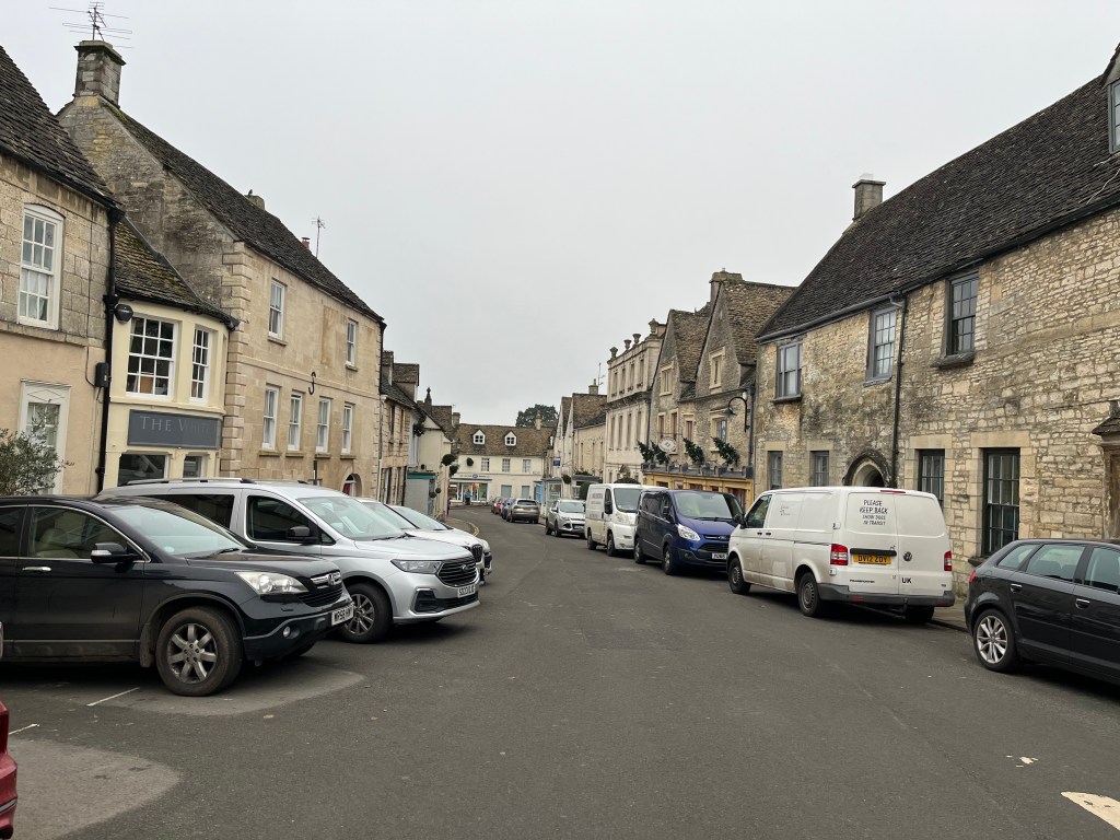 Minchinhampton in the Cotswalds. Cotswald stone buildings with cars parked along the street.