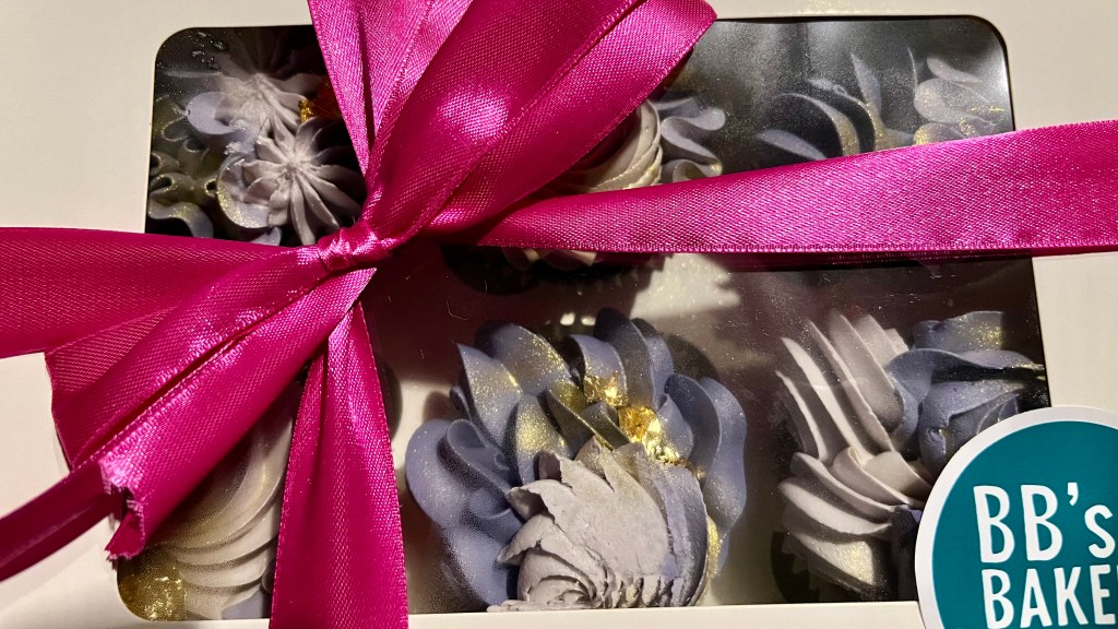 a box of frosted cupcakes with a magenta bow on top