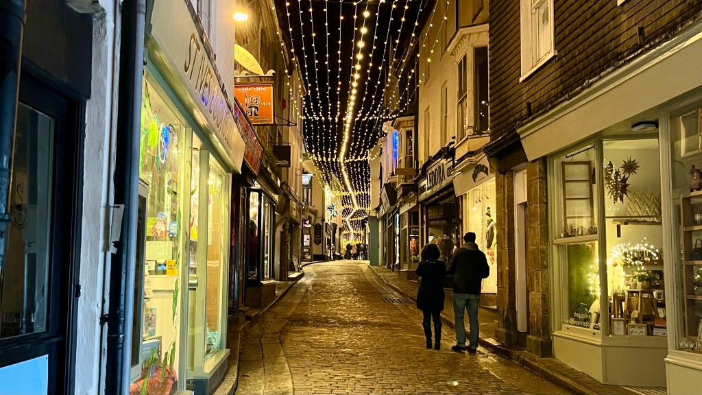 a long, narrow street at night with shops on both sides and fairy lights above the street.