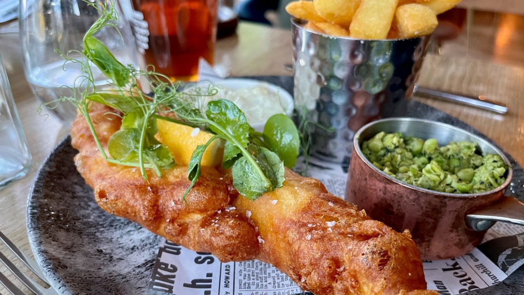a piece of battered fish with mushy peas and fried potatoes