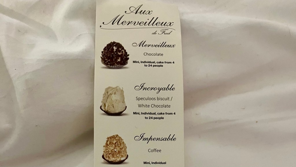 part of a card showing three small cakes sold at Aux Merveilleux by Fred including chocolate, white chocolate and coffee.
